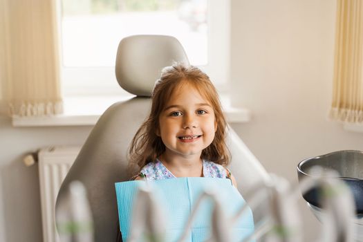 Happy child patient of dentistry. Teeth treatment. Attractive kid girl sitting in dental office and smiling. Child at dentist visiting