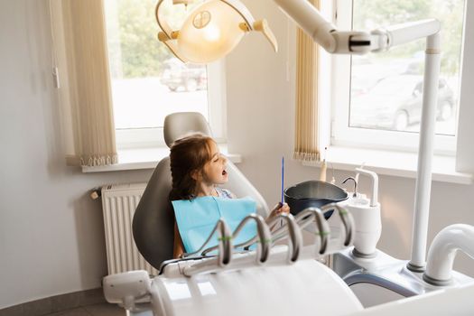 Child looking in the mirror at the dentist. Happy child patient of dentistry. Teeth treatment. Attractive kid girl sitting in dental office and smiling