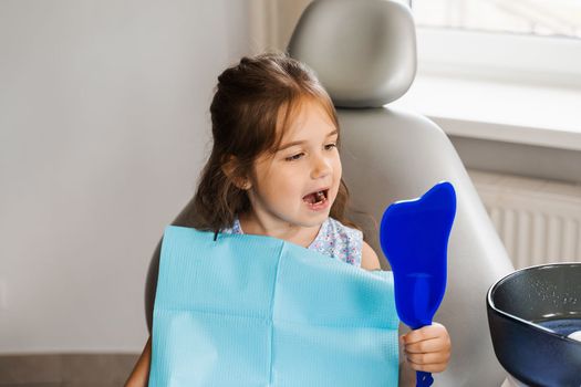 Teeth treatment. Child looking in the mirror at the dentist. Happy child patient of dentistry. Attractive kid girl sitting in dental office and smiling