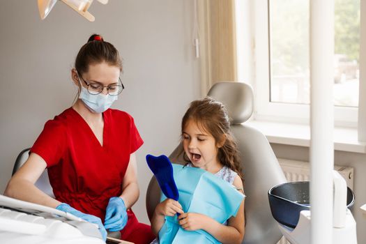 Consultation with child dentist at dentistry. Teeth treatment. Child looking in the mirror at the dentist. Happy child patient of dentistry