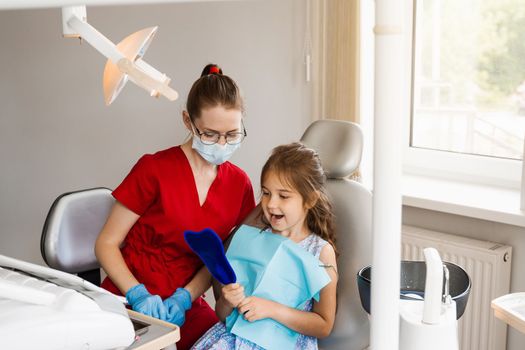 Consultation with child dentist at dentistry. Teeth treatment. Child looking in the mirror at the dentist. Happy child patient of dentistry