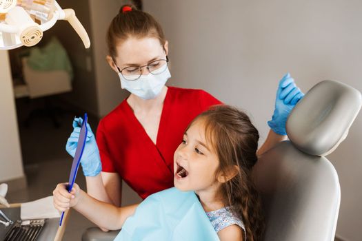 Consultation with child dentist at dentistry. Teeth treatment. Child looking in the mirror at the dentist. Happy child patient of dentistry