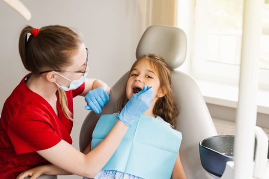 Pediatric dentist examines teeth of child girl for treatment of toothache. Pain in teeth in children. Consultation with pediatric dentist in dentistry