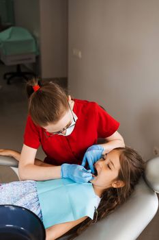 Consultation with child dentist at dentistry. Teeth treatment. Children dentist examines girl mouth and teeth and treats toothaches. Happy child patient of dentistry