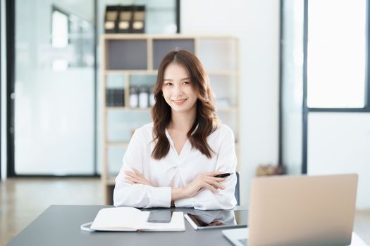 Portrait of a woman business owner showing a happy smiling face as he has successfully invested her business using computers and financial budget documents at work.