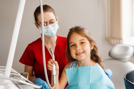 Cheerful girl child holding dental drill and smiling in dentistry. The child smiles at the consultation with the dentist