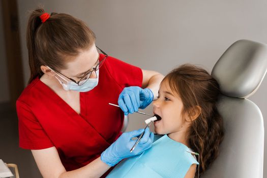 Pediatric dentist puts cotton swab in mouth of a child girl to install a photopolymer dental filling and treat teeth