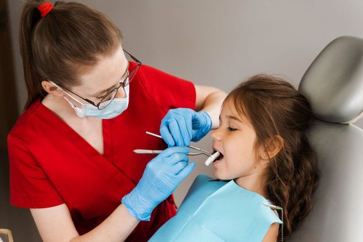 Pediatric dentist puts cotton swab in mouth of a child girl to install a photopolymer dental filling and treat teeth