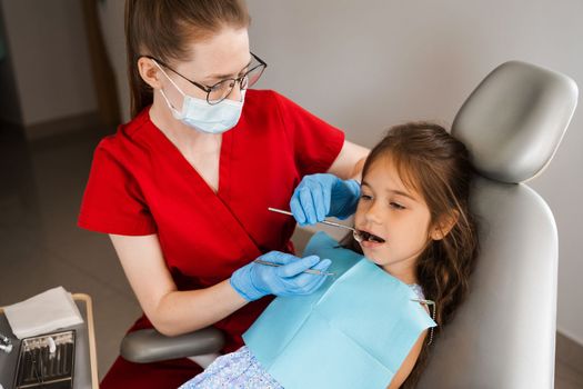 Pediatric dentist examines child girl mouth and teeth and treats toothaches. Happy child patient of dentistry. Consultation with child dentist at dentistry. Teeth treatment