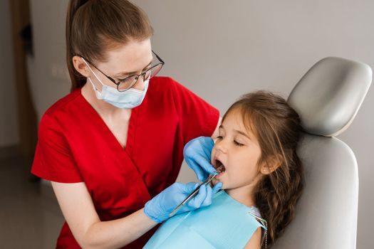 Pediatric dentist examines child girl mouth and teeth and treats toothaches. Happy child patient of dentistry. Consultation with child dentist at dentistry. Teeth treatment