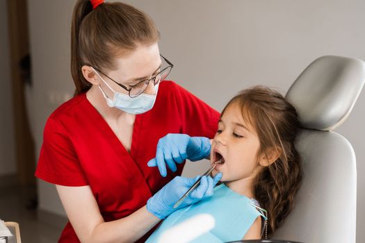Pediatric dentist examines child girl mouth and teeth and treats toothaches. Happy child patient of dentistry. Consultation with child dentist at dentistry. Teeth treatment