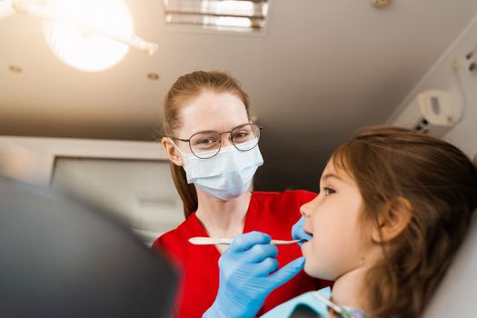 Pediatric dentist examines child girl mouth and teeth and treats toothaches. Happy child patient of dentistry. Consultation with child dentist at dentistry. Teeth treatment