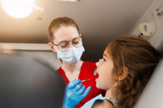 Pediatric dentist examines child girl mouth and teeth and treats toothaches. Happy child patient of dentistry. Consultation with child dentist at dentistry. Teeth treatment