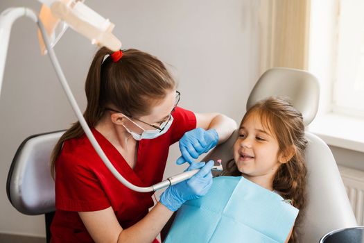 Professional hygiene for teeth of child in dentistry. Professional teeth cleaning for child girl. Pediatric dentist examines and consults kid patient in dentistry