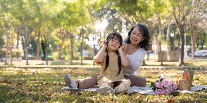 Happy Asian grandmother picnicking with her lovely granddaughter in park together. leisure and family concept.