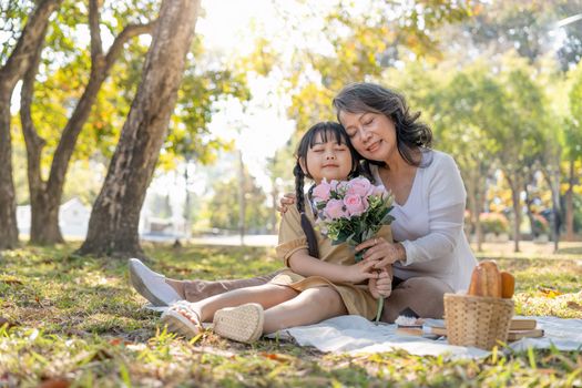 Happy Asian grandmother hugging with her lovely granddaughter in park together. leisure and family concept.