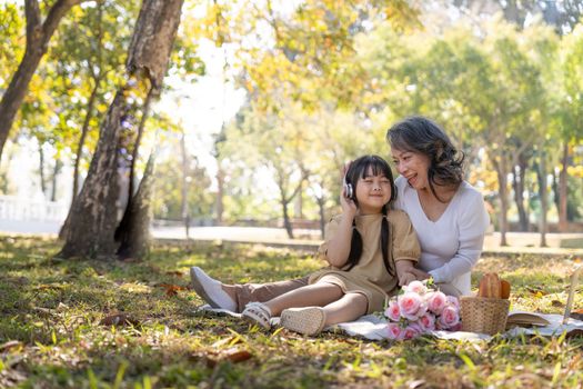Happy Asian grandmother picnicking with her lovely granddaughter in park together. leisure and family concept.