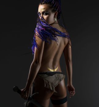 Sexy resolute woman with dreadlocks topless holding a sword in her hand in the image of amazon rearview on gray background