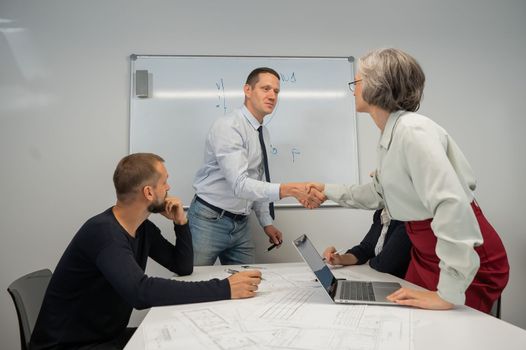 The boss makes a presentation to subordinates at the white board. Caucasian man shaking hands with middle aged woman