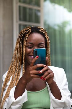 Happy young African American woman with braided hair using mobile phone. Vertical image. Technology and lifestyle.