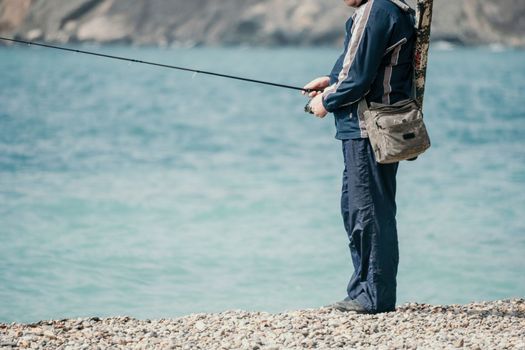 Man hobby fishing on sea tightens a fishing line reel of fish summer. Calm surface sea. Close-up of a fisherman hands twist reel with fishing line on a rod. Fishing in the blue sea outdoors