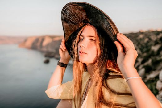 Portrait of happy young woman wearing summer black hat with large brim at beach on sunset. Closeup face of attractive girl with black straw hat. Happy young woman smiling and looking at camera at sea