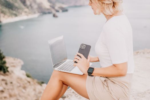 Digital nomad, Business woman working on laptop by the sea. Pretty lady typing on computer by the sea at sunset, makes a business transaction online from a distance. Freelance remote work on vacation