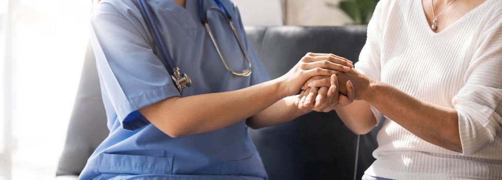 Closeup Happy patient is holding caregiver for a hand while spending time together. Elderly woman in nursing home and nurse...