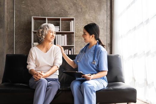 Happy patient is holding caregiver for a hand while spending time together. Elderly woman in nursing home and nurse...