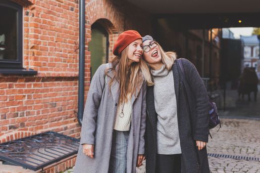 Young pretty girls friends having fun outdoor in autumn evening in city laughing and going crazy on the street - friendship and funny people