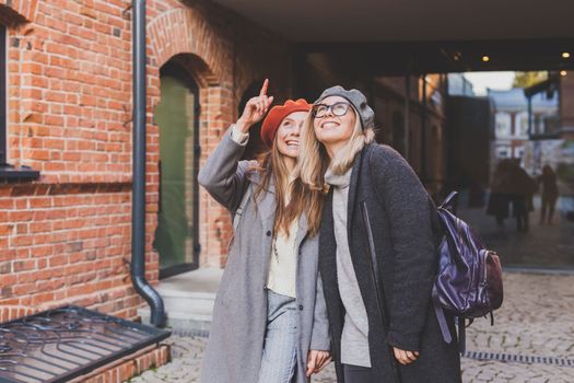 Young pretty girls friends having fun outdoor in autumn evening in city laughing and going crazy on the street - friendship and funny people