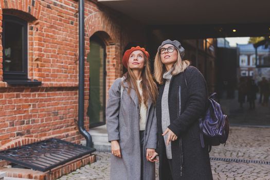 Young pretty girls friends having fun outdoor in autumn evening in city laughing and going crazy on the street - friendship and funny people