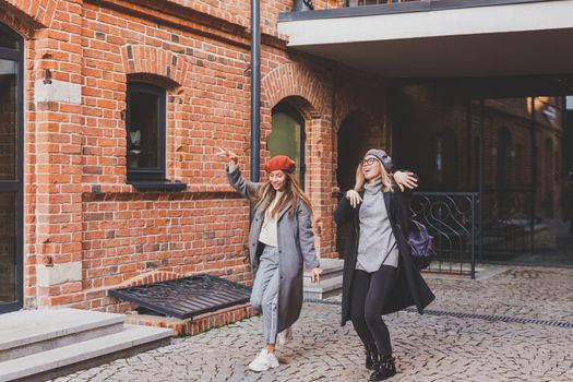 Young pretty girls friends having fun outdoor in autumn evening in city laughing and going crazy on the street - friendship and funny people