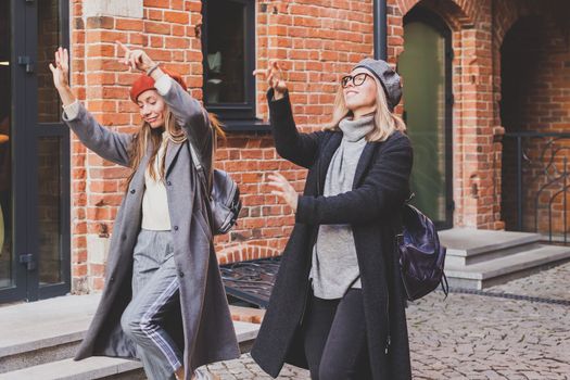 Young pretty girls friends having fun outdoor in autumn evening in city laughing and going crazy on the street - friendship and funny people