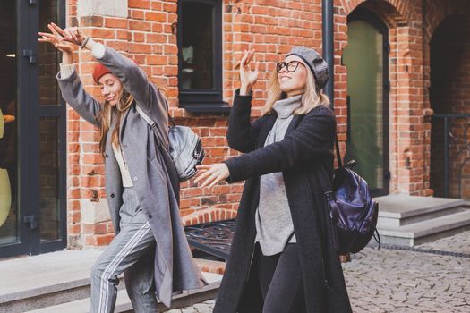 Young pretty girls friends having fun outdoor in autumn evening in city laughing and going crazy on the street - friendship and funny people