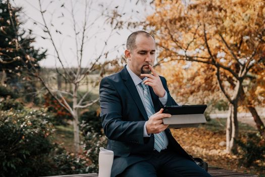 Mature entrepreneur drink coffee in autumn park. Senior executive rest in city park.