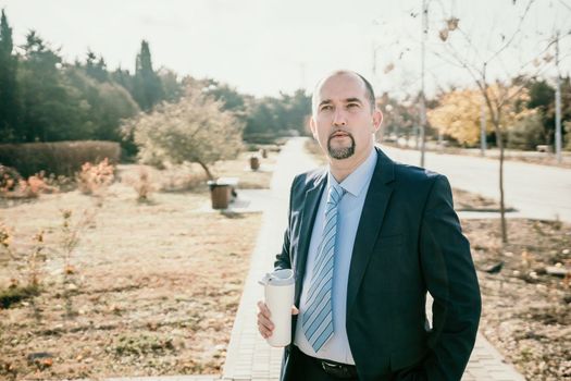 Mature entrepreneur drink coffee in autumn park. Senior executive rest in city park.