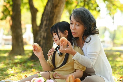 Loving grandmother and little cute girl child having fun relaxing together in the park. Family, generation and people concept.