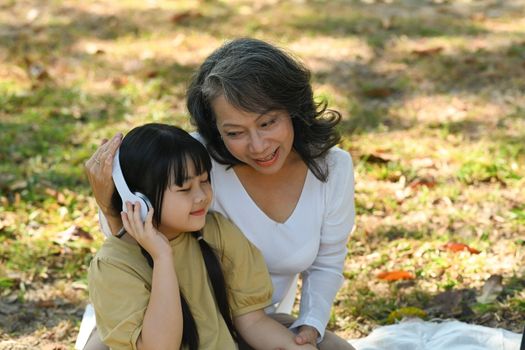 Pleasant middle aged grandma and little girl relaxing, spending time outdoors in sunny summer garden. Family and generation concept.