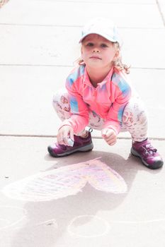 Little girl playing with chalk on a driveway in front of the house.