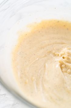 Mixing ingredients in a large glass mixing bowl to make dressing for macaroni salad with chicken.