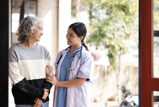 Young caregiver helping senior woman walking. Nurse assisting her old woman patient at nursing home. Senior woman with walking stick being helped by nurse at home...