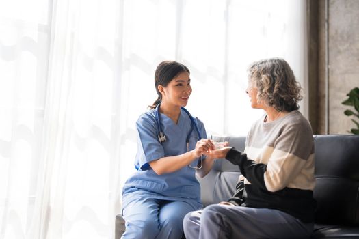 Young caregiver helping senior woman walking. Nurse assisting her old woman patient at nursing home. Senior woman with walking stick being helped by nurse at home...