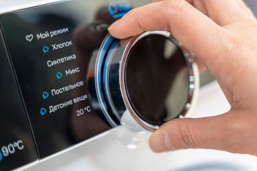 a woman's hand selects the washing mode with a round selector on the control panel of a modern washing machine. technologies. close-up. choosing a washing program