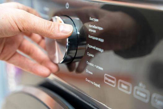 a woman's hand selects the washing mode with a round selector on the control panel of a modern washing machine. technologies. close-up. choosing a washing program