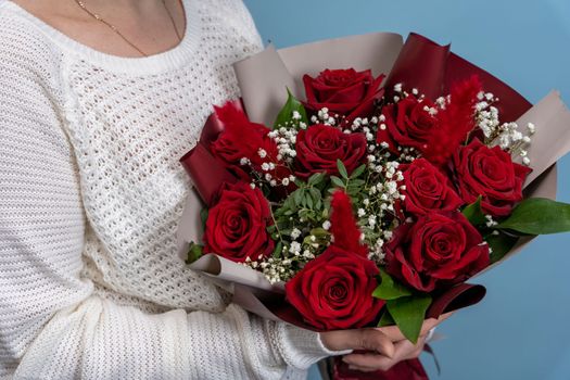 a beautiful bouquet of fresh red roses in women's hands on a light blue background. Congratulations on Mother's Day. valentine's day. wedding