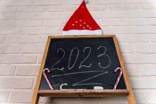 a black slate decorated with candy in the form of a caramel cane. The year 2023 is written in chalk on the blackboard. Happy New Year. 2023. Number written in chalk on a school board