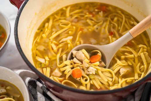 Serving chicken noodle soup with kluski noodles in white ceramic soup bowls.