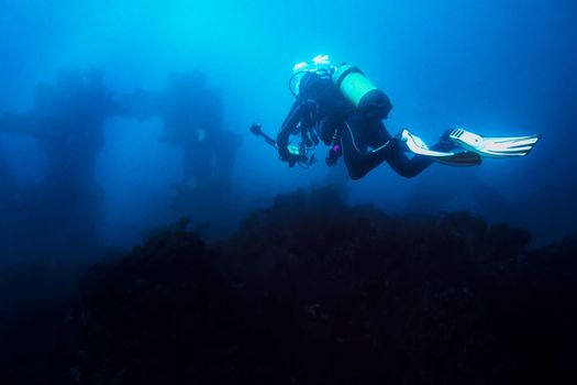 diver with his camera taking a dive through the blue sea towards the wreck. The old remains of the ship look distant and blurred giving an aura of mystery
