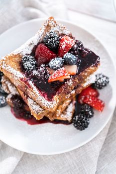 Stack of freshly made french toast garnished with mix berry compote and powder sugar.